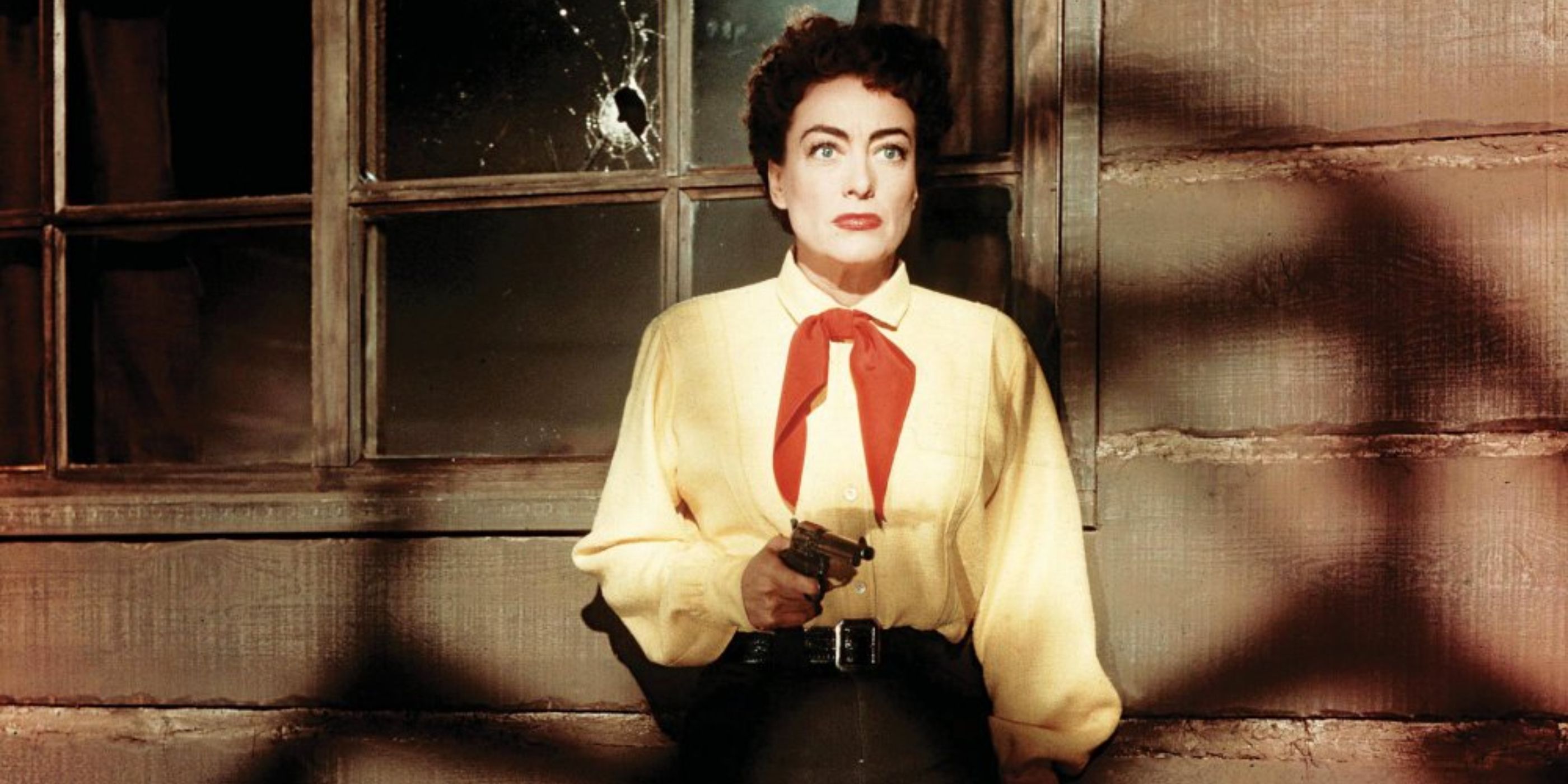 Vienna (Joan Crawford) stands in shadows with a yellow shirt aiming a revolver in 'Johnny Guitar'