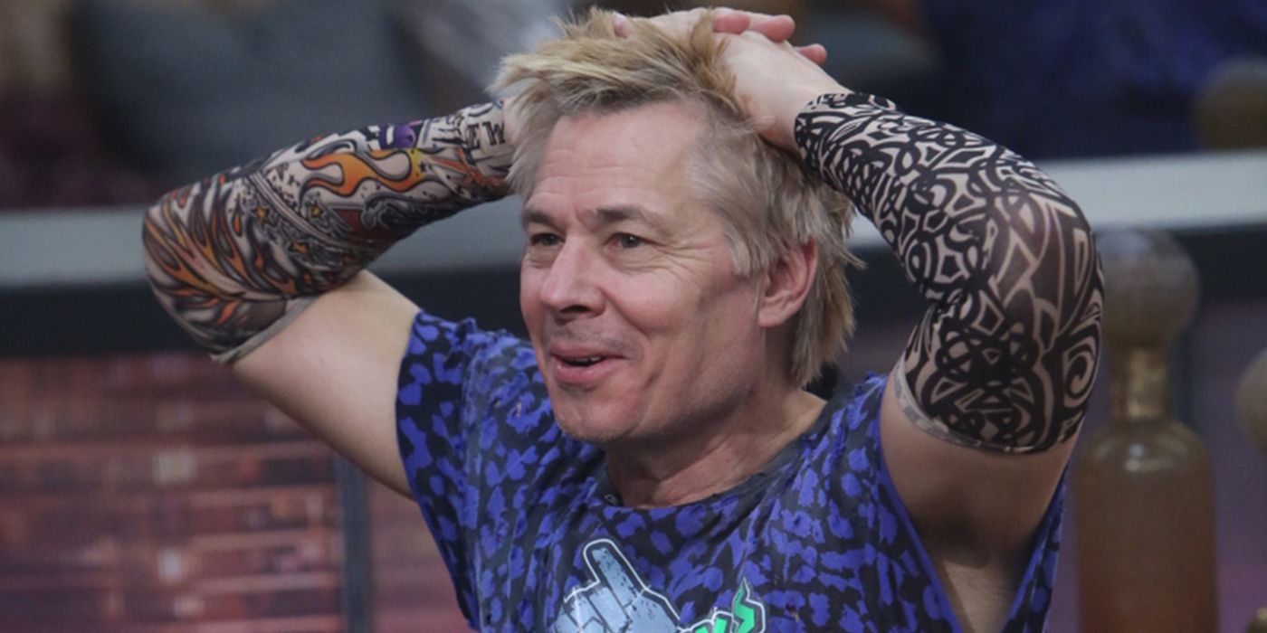 Kate Kaelin on Celebrity Big Brother looking shocked, hands on his head with tattoo sleeves on his arms.