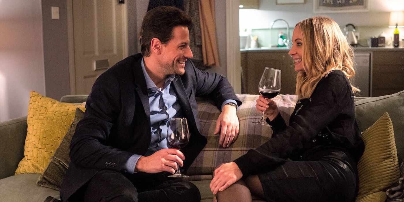 A man and a woman laughing together on a couch drinking wine in a scene from Liar.