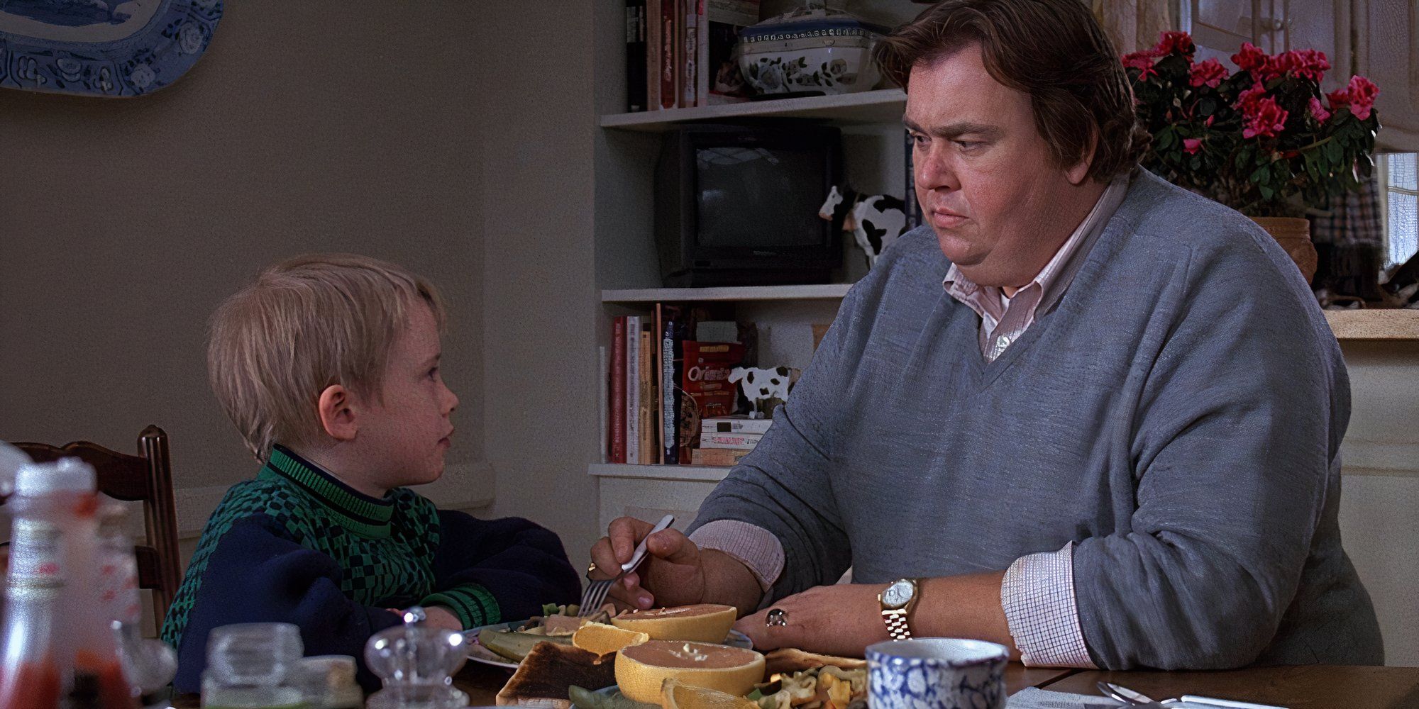 Macaulay Culkin sitting at a table looking at John Candy sitting next to him in Uncle Buck (1989)