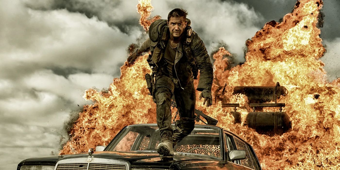 Max (Tom Hardy) standing on top of a car facing the camera and preparing to jump as something explodes behind him in Mad Max: Fury Road