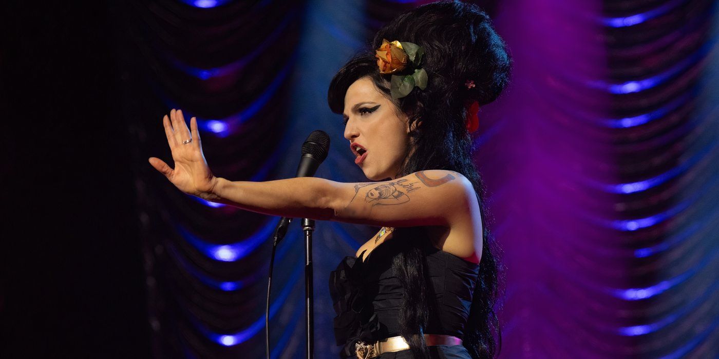 Marisa Abela performing on stage as Amy Winehouse, sticking her arm out with her hand up.