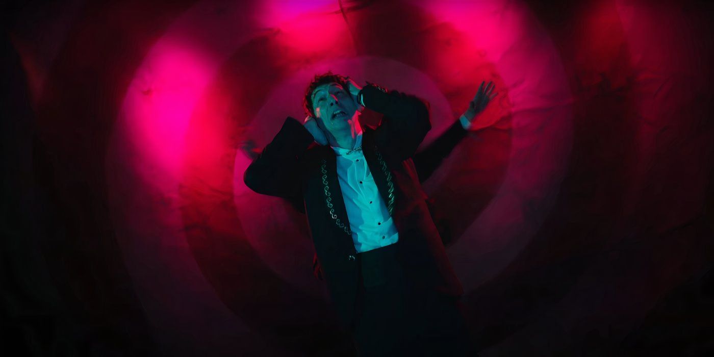 Adam Driver in a suit, holding his hands up to his ears while falling into a red-lit spiral.