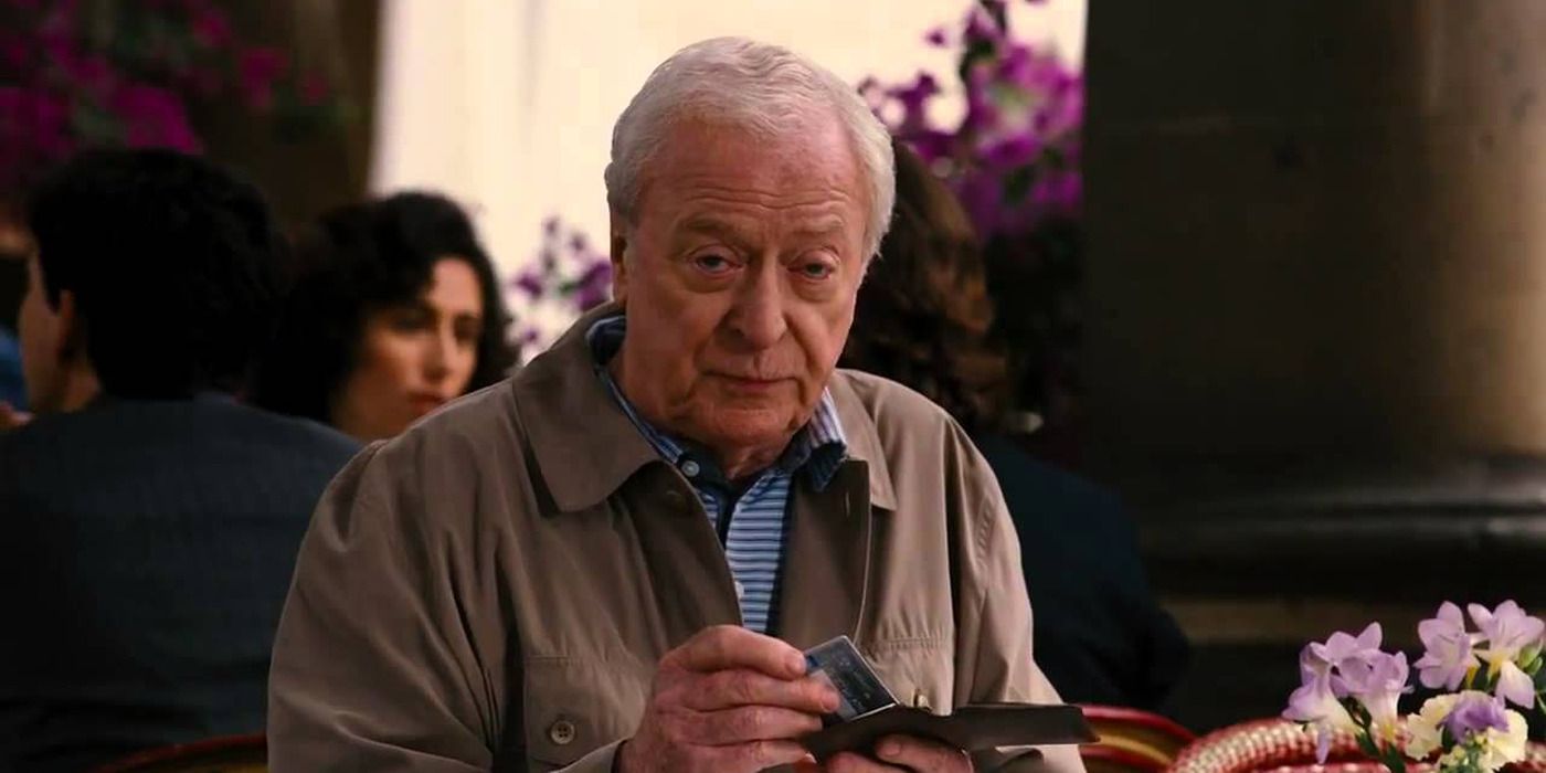 Alfred in a restaurant looking intently at someone off-camera in 'The Dark Knight Rises'