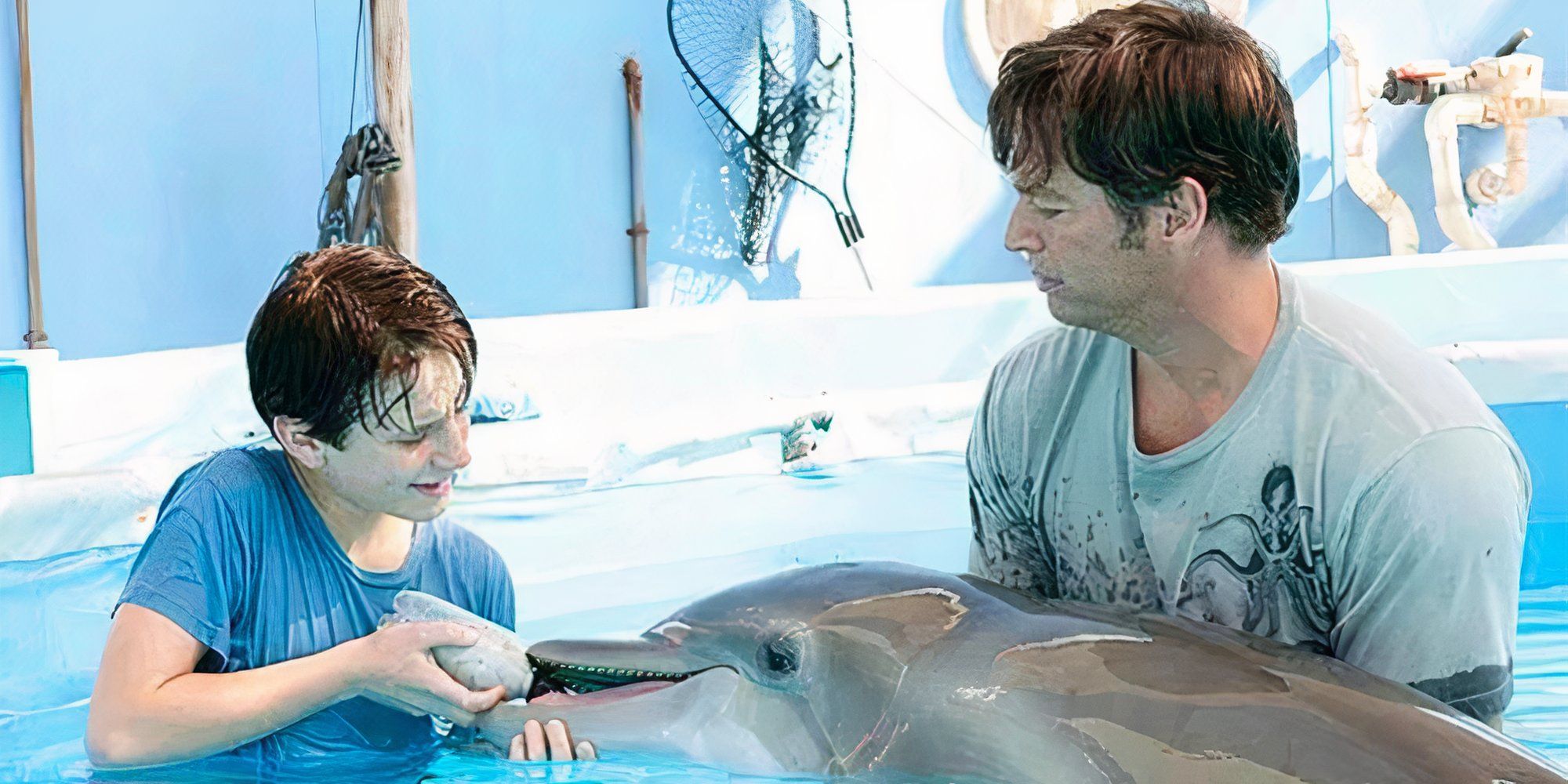 Nathan Gamble giving a dolphin a bottle while Harry Connick Jr. holds him in the water in Dolphin Tale (2011)