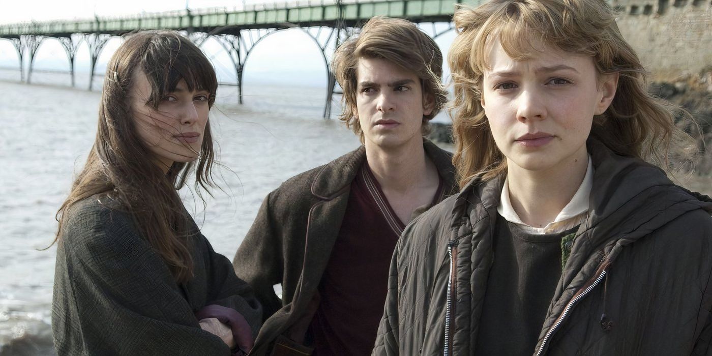From left to right: Ruth (Keira Knightley), Tommy (Andrew Garfield), and Kathy (Carey Mulligan) stare forlornly at the camera with a bridge over water in the background