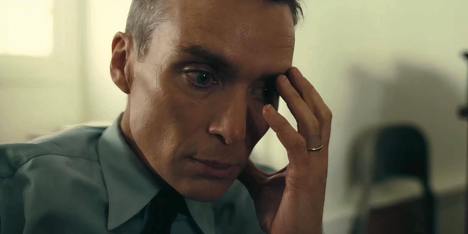 J. Robert Oppenheimer, played by actor Cillian Murphy, clutches his face, overcome by dread in Oppenheimer.