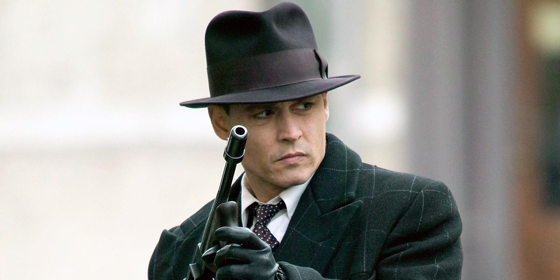 Johnny Depp stands in the street in typical 1930s gangster attire, holding a machine gun 