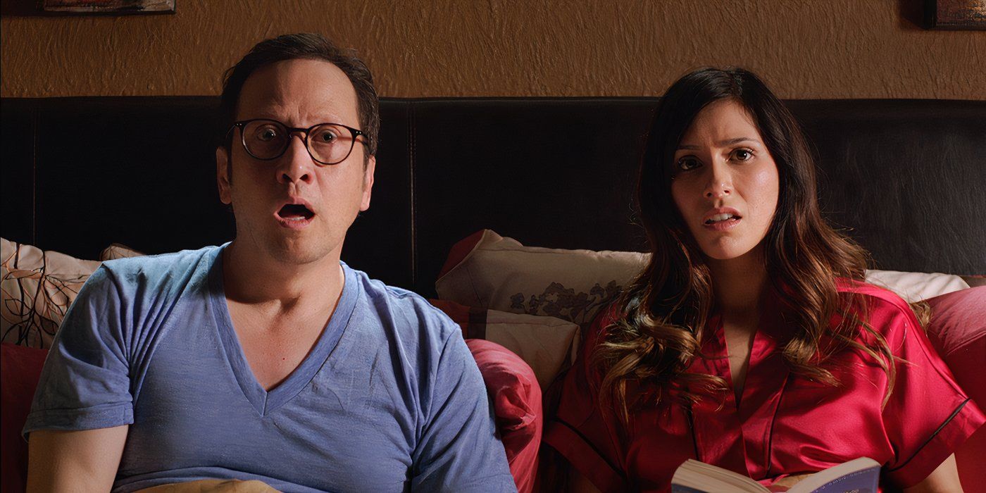 Rob Schneider and his wife in bed looking shocked, mouths agape in a scene from Real Rob.