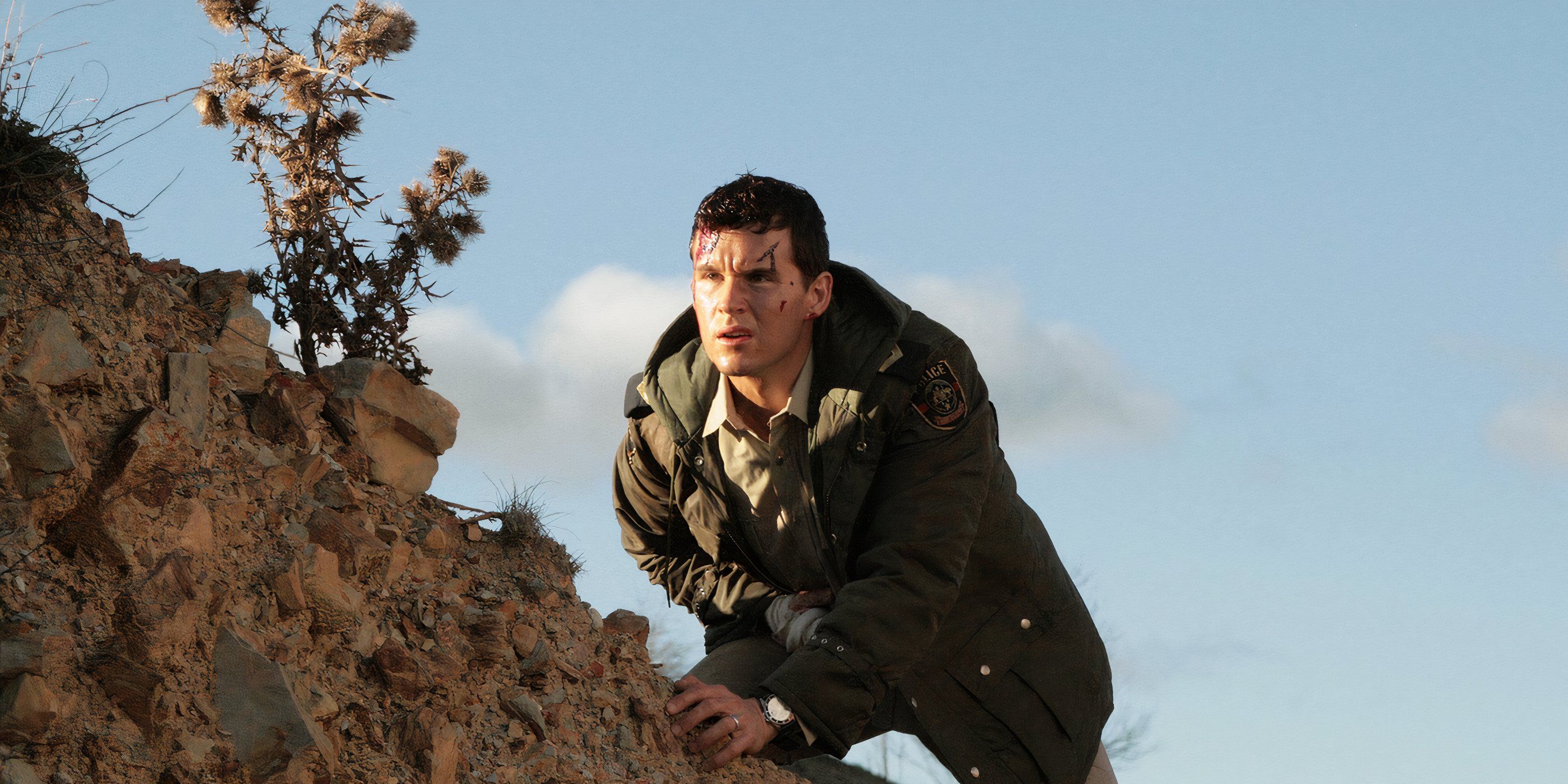 Police officer Shane Cooper (Ryan Kwanten) climbs a rocky hill will nursing a wounded hand as blood streams from his face in 'Red Hill' (2010).