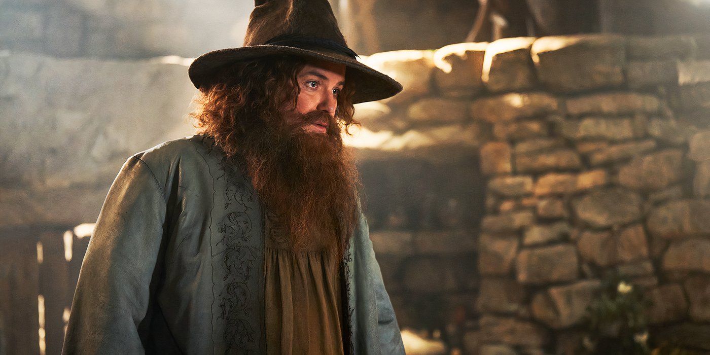 Rory Kinnear como Tom Bombadil con su túnica azul mirando hacia abajo en The Rings of Power