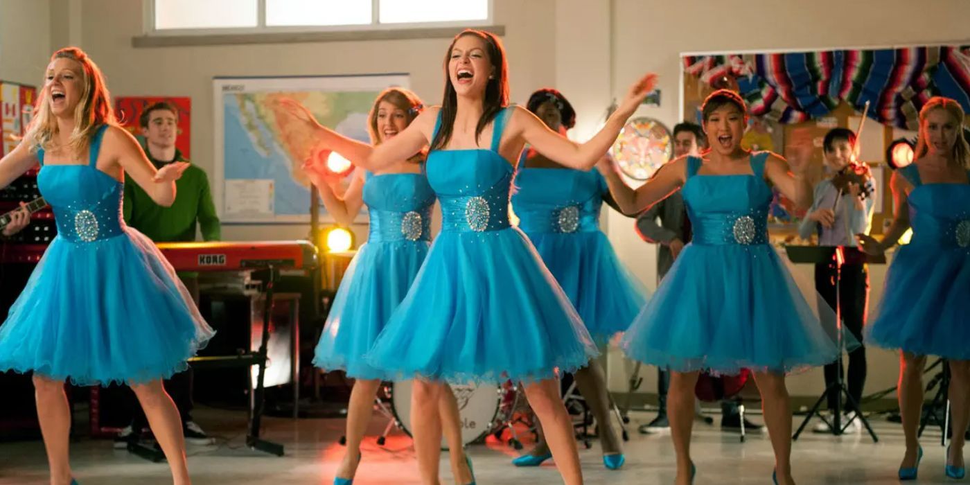 Brittney, Marley, Tina, and the rest of the Glee club girls, wearing light blue dresses and matching heels, perform "Tell Him" in the Glee Club room.