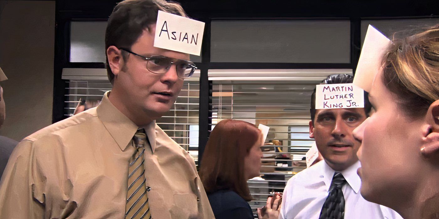 Dwight (Rainn Wilson) wearing a note on his head that says "Asian," talking to Pam (Jenna Fischer) while Michael (Steve Carell) watches on The Office