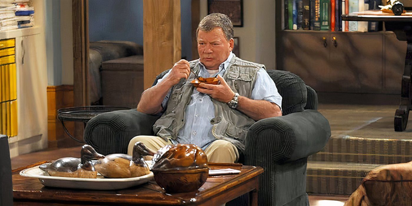 William Shatner sitting in a chair in a living room eating with a fisherman&rsquo;s vest on in S#*! My Dad Says.