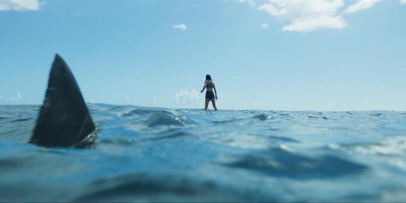 A shark circles Hiftu Quasem's Meg as she stands on a rock in the ocean in Something in the Water.