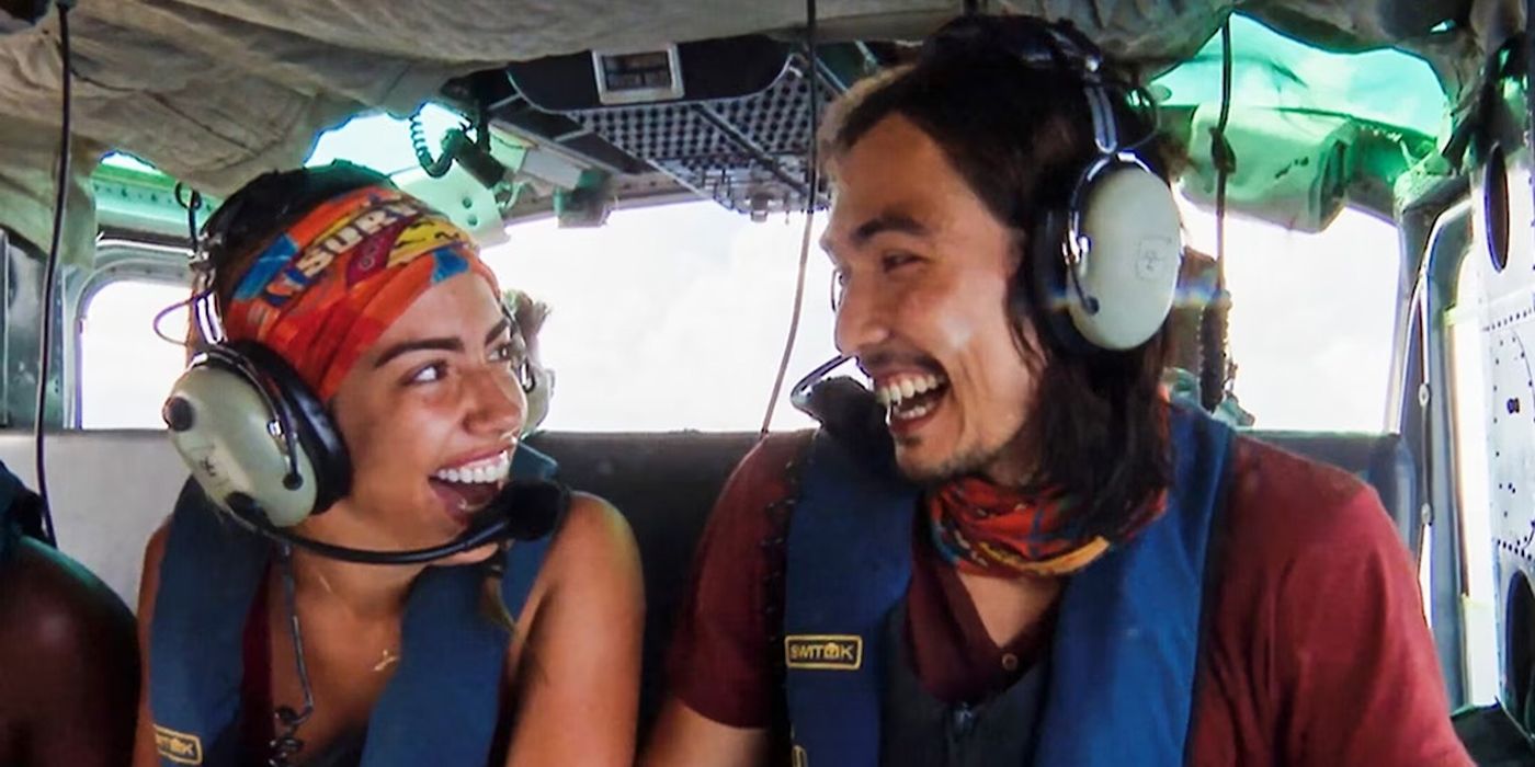 Dee and Austin from Survivor in a helicopter during a reward, looking at one another and smiling.