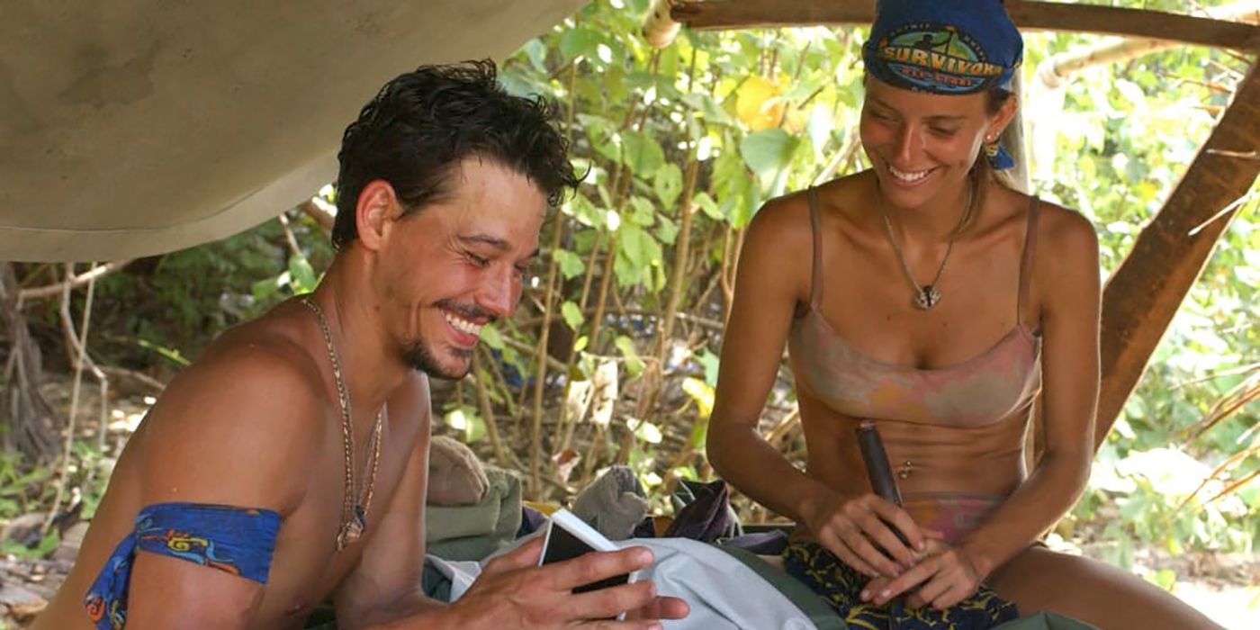 Rob and Amber under the shelter on Survivor, smiling and laughing.