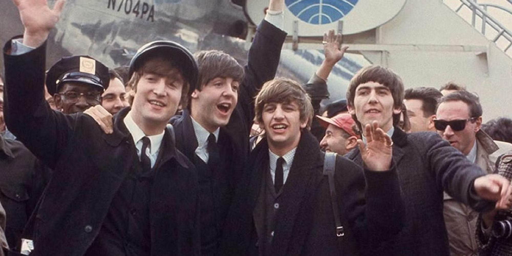 The Beatles posing and waving in front of a building and a crowd of people