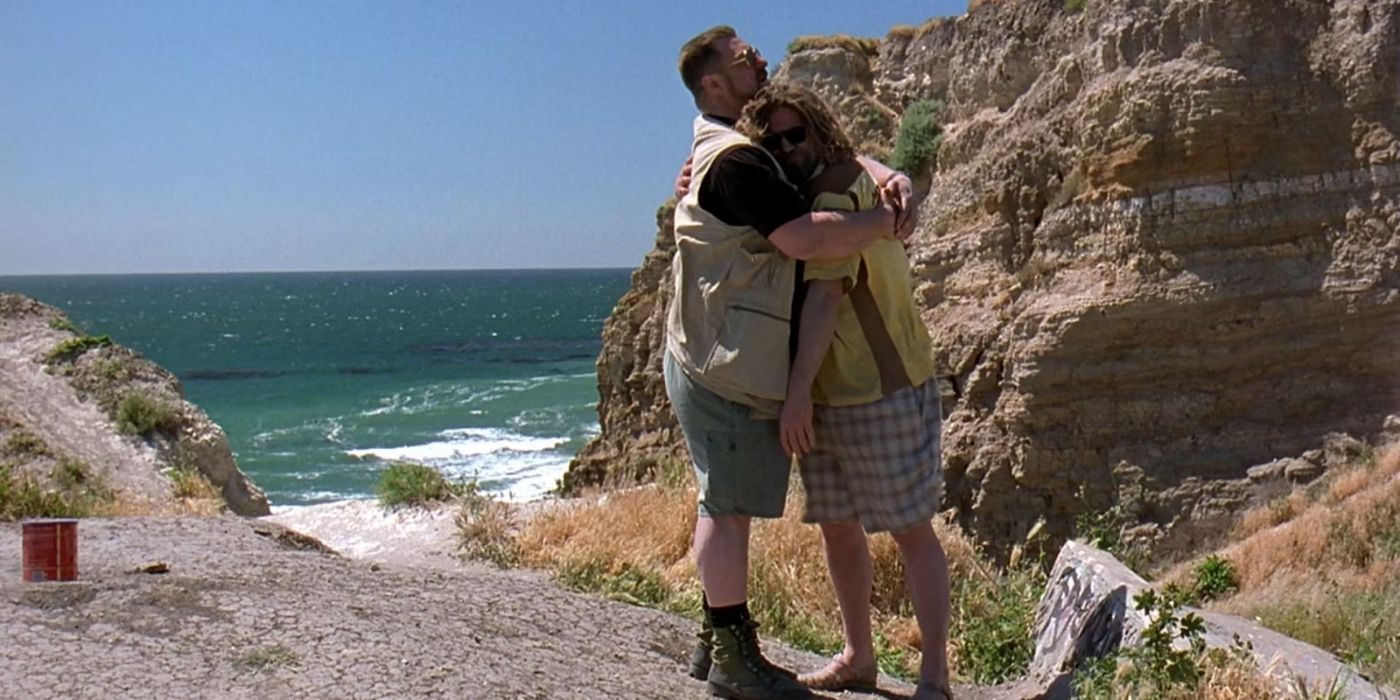 Walter Sobchak (John Goodman) hugs the Dude (Jeff Bridges) on a sunny day by the beach with the container holding Donny's ashes resting behind him in 'The Big Lebowski' (1998).