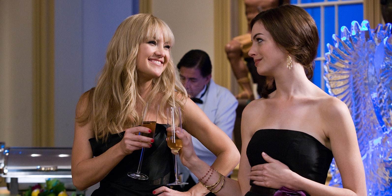 Kate Hudson and Anne Hathaway smile at each other and drink champagne in fancy dresses in Bride Wars.