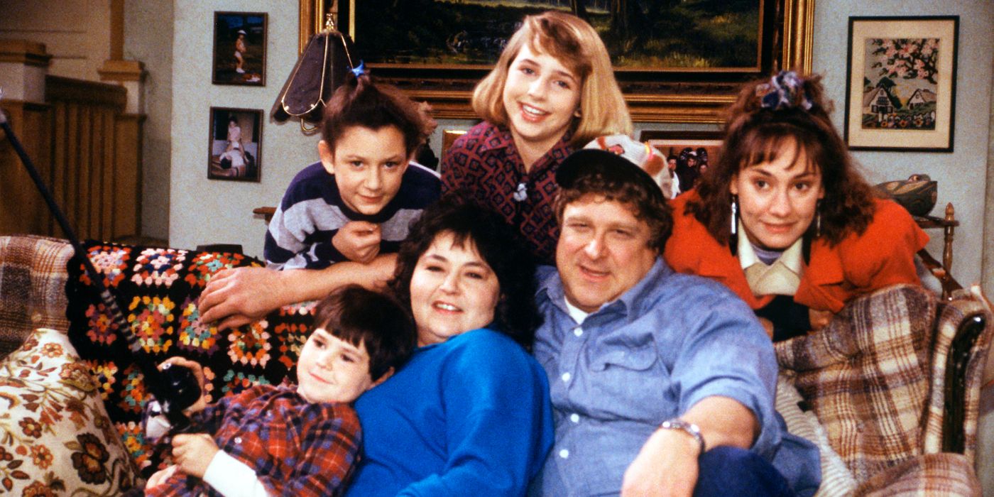 The cast of Roseanne sitting on a couch in the living room posing