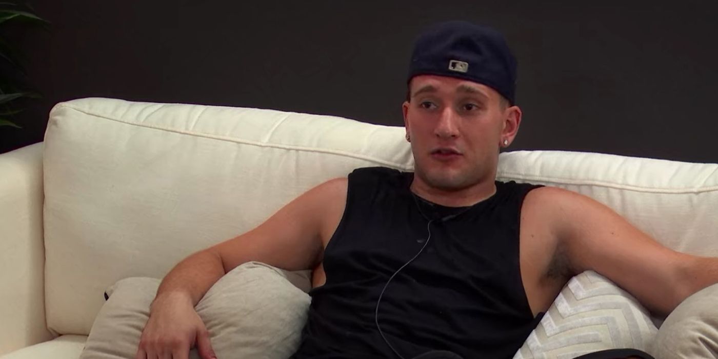 Joey from The Circle sprawled out on the couch wearing a black tank top and black hat backwards.