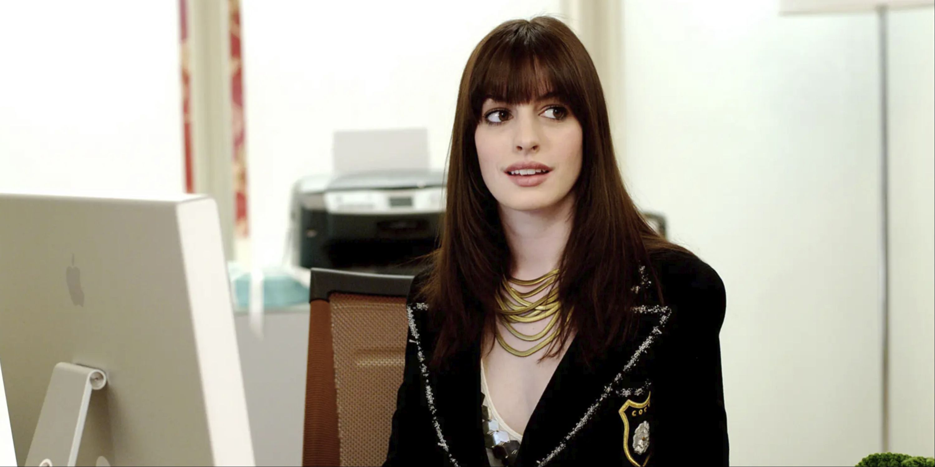 Anne Hathaway sitting at a desk and looking to her left as Andy in The Devil Wears Prada.
