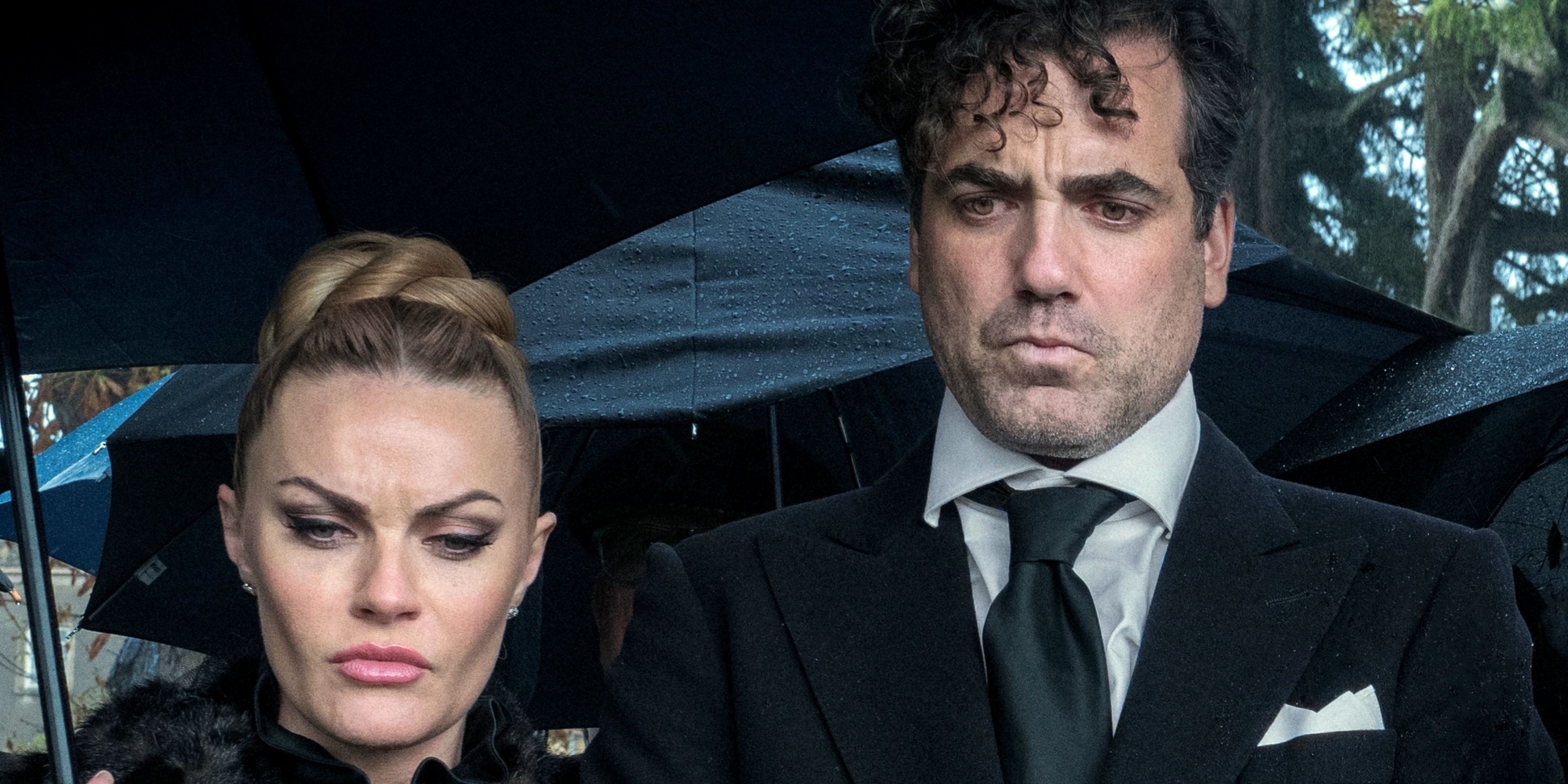 Daniel Ings as Freddy with Chanel Cresswell under umbrellas at a funeral in The Gentlemen