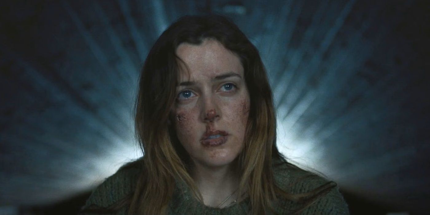 Grace, bruised and weary, standing in front of a beam of light, in The Lodge (2019)