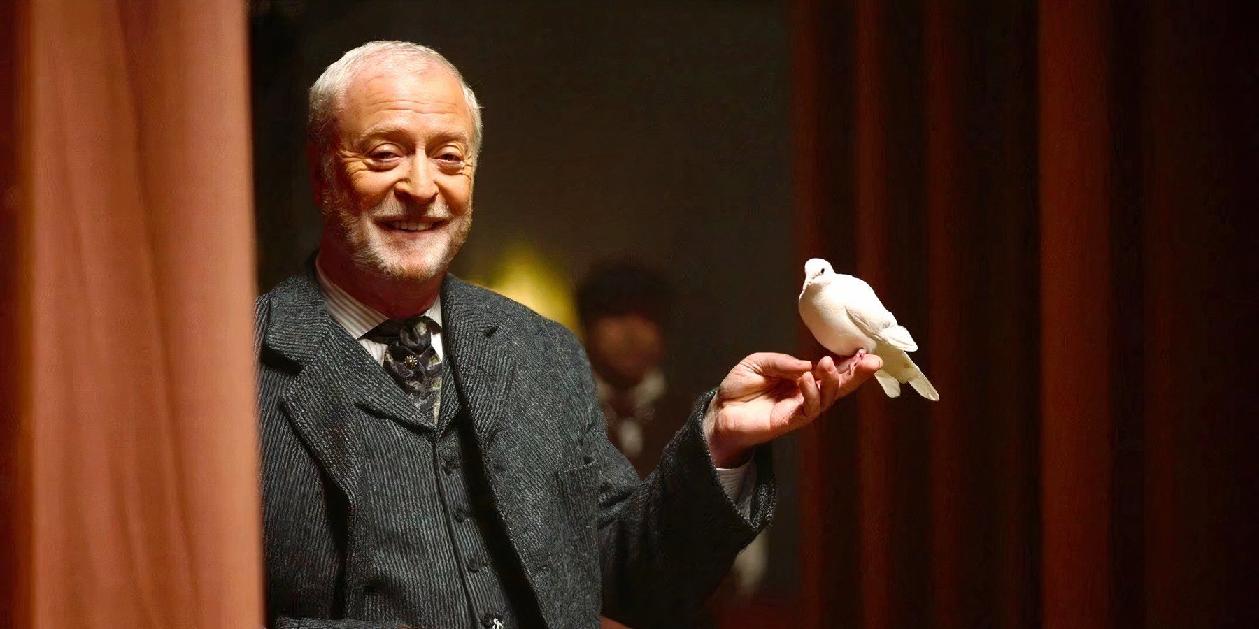 Cutter (Michael Caine) stands in the wings of a theater, holding a dove perched on one hand in The Prestige.