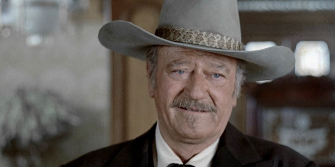 A close up of John Wayne smiling in a cowboy hat in The Shootist