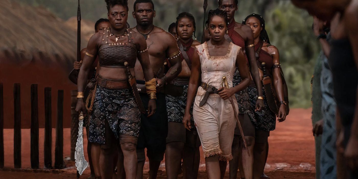 A group of Agojie warriors walks through their village with their hands on their sheathed swords 