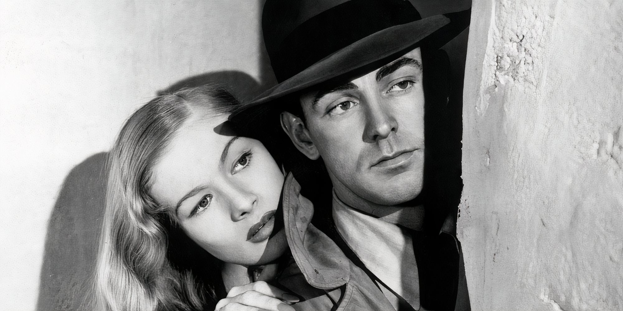 Veronica Lake and Alan Ladd looking from behind a wall in This Gun for Hire (1942) 