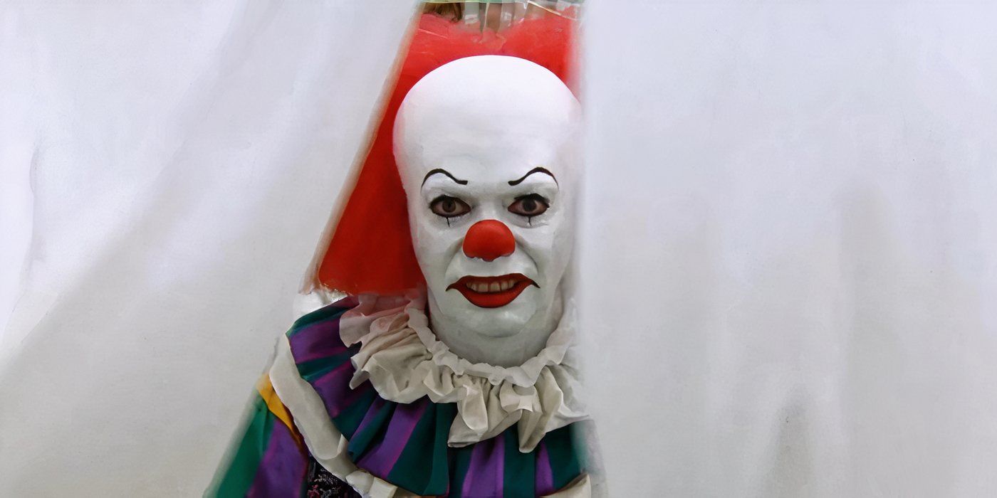 An angry-looking Pennywise (Tim Curry) stares from between hanging sheets in 1990&rsquo;s It