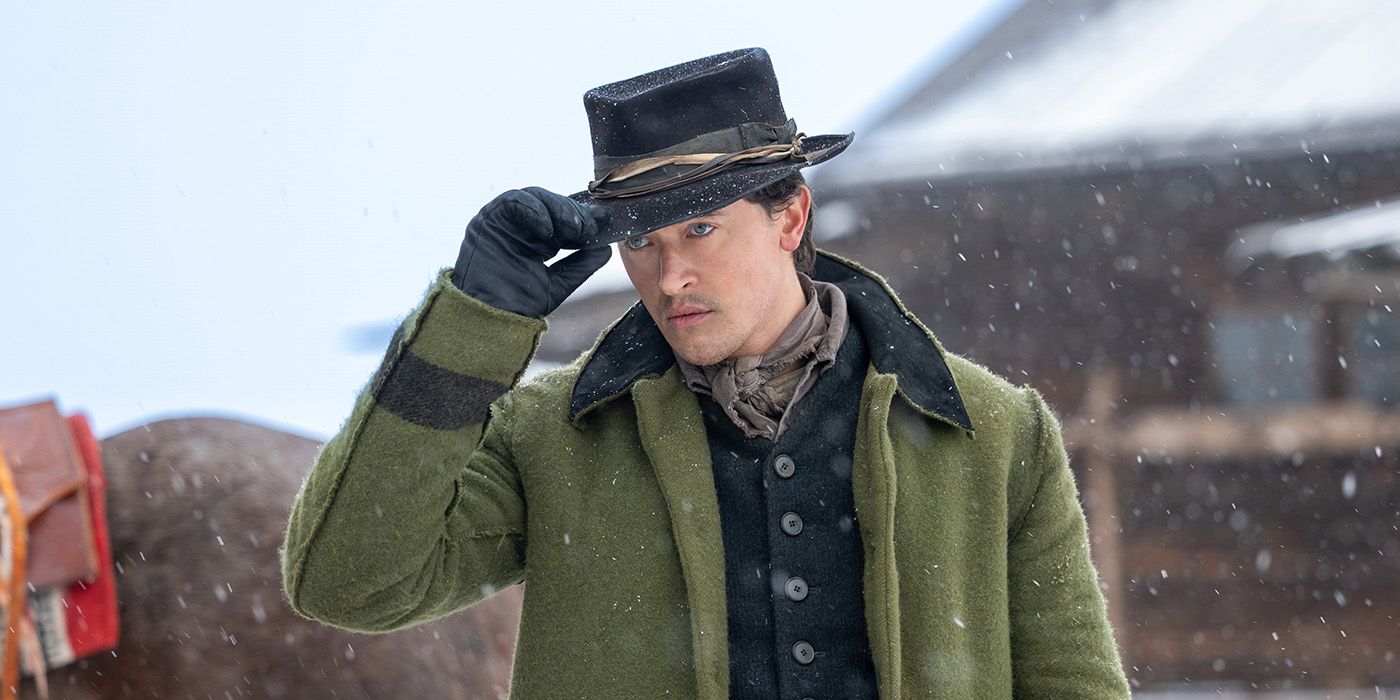 Tom Blyth as Billy the Kid tipping his hat and wearing a green jacket in a snowy landscape