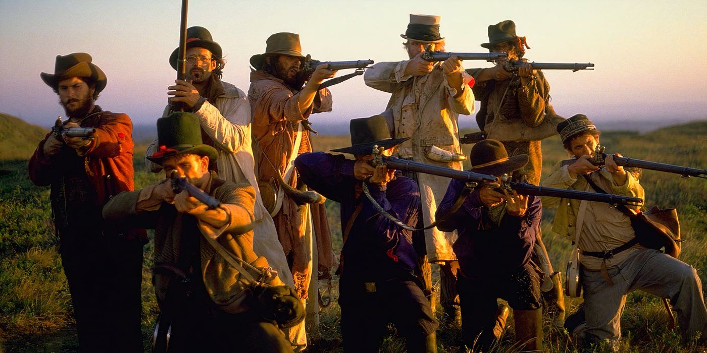 A group of nine cowboys aims their guns slightly to the right of the camera