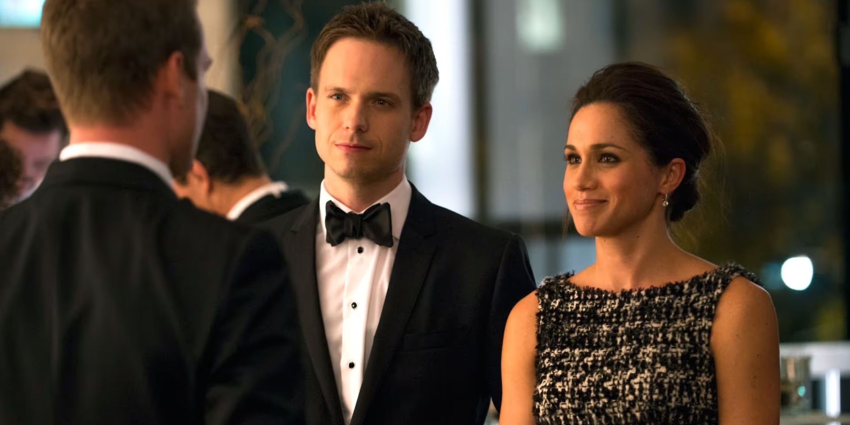Mike Ross (Patrick J. Adams) and Rachel Zane (Meghan Markle) stand next to each other while talking to someone at a fancy dress event in 'Suits'.