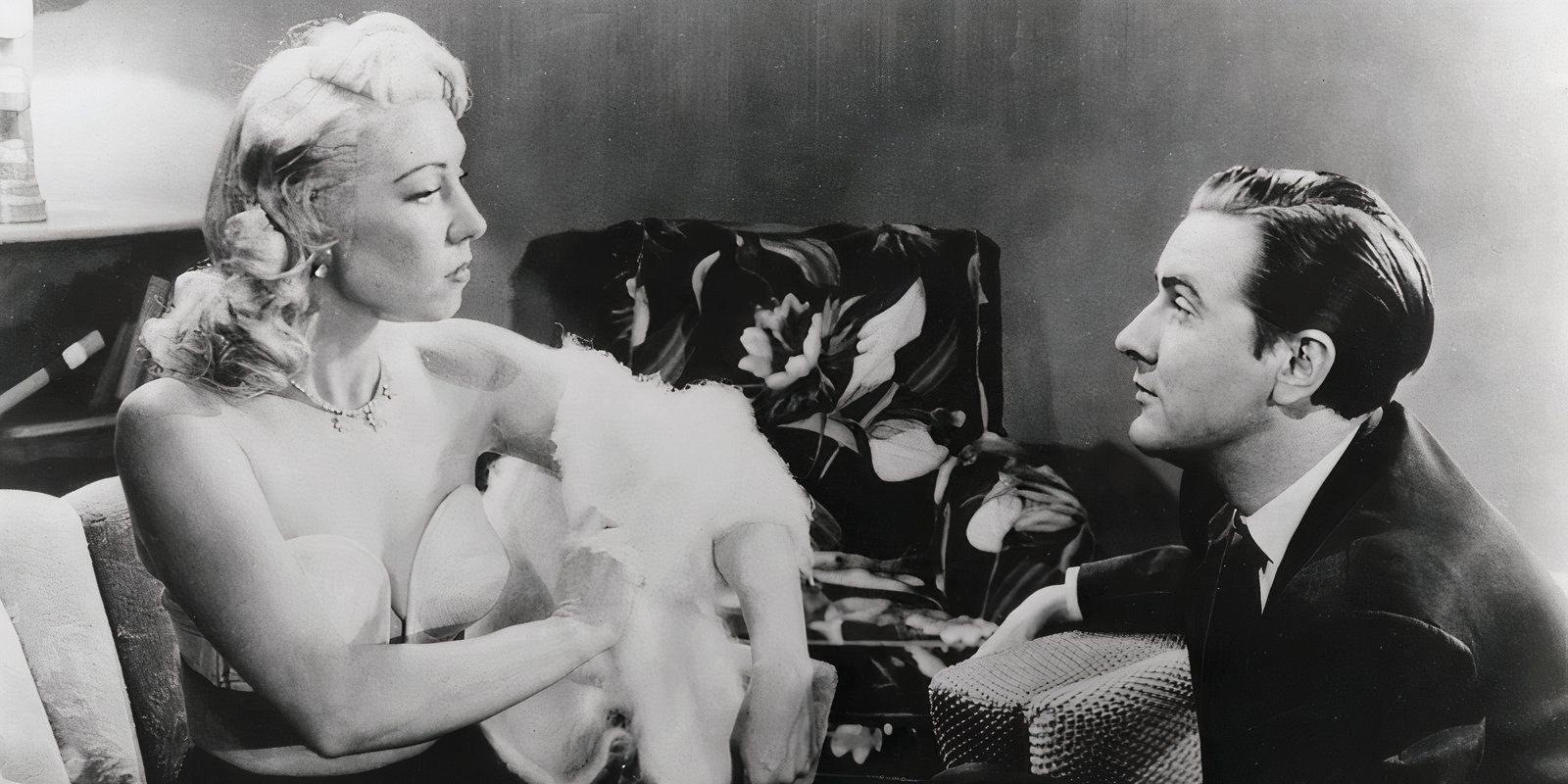 Woman taking her fur coat off in front of a keeling Ed Wood in 'Glen or Glenda'