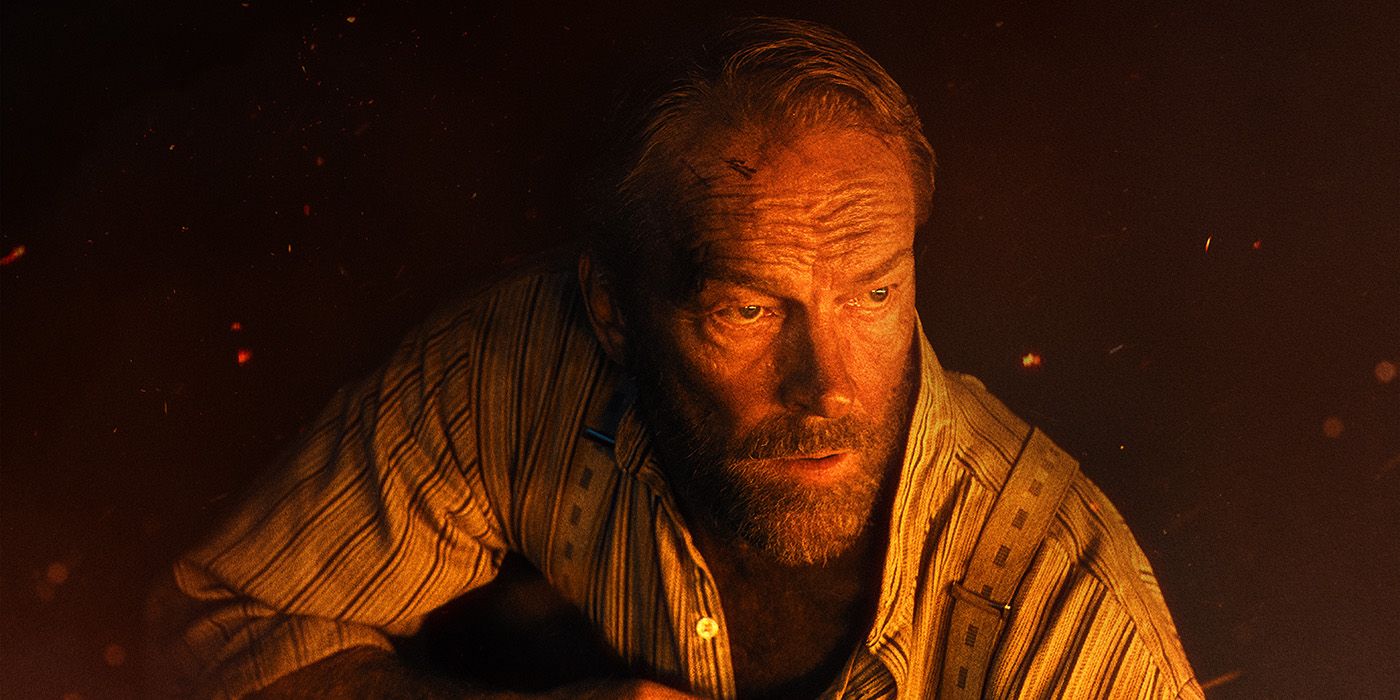 Iain Glen lit by firelight and holding a rifle in The Last Front