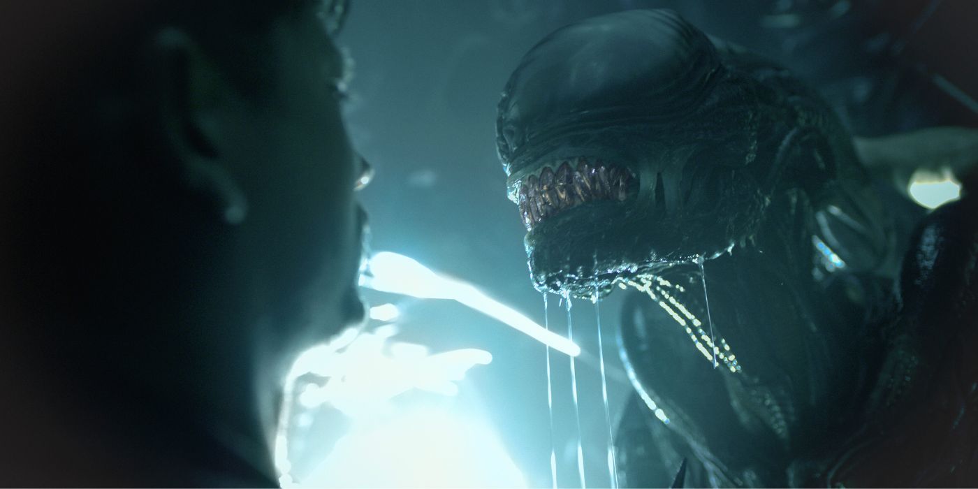 A Xenomorph drooling while towering over a cowering human in Alien: Romulus.