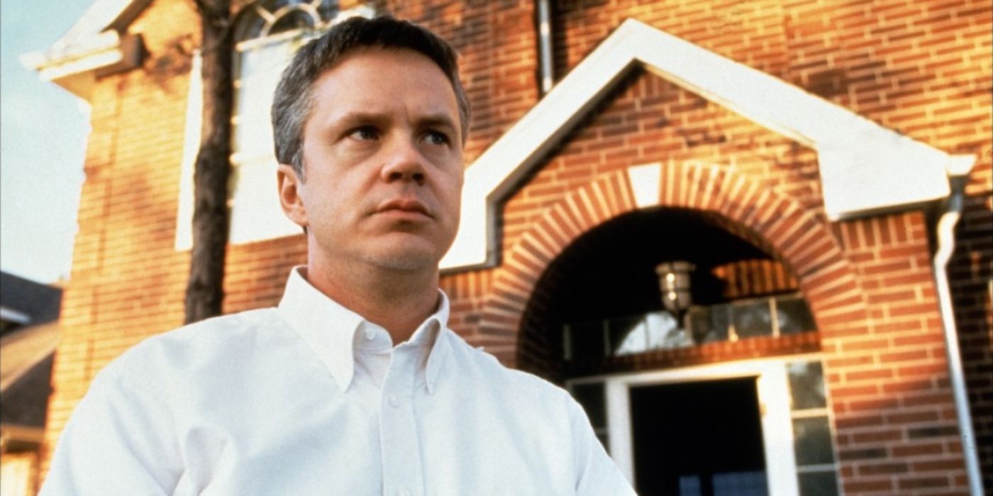 Oliver Land (Tim Robbins) casts a blank glare as he stands in a white shirt out the front of a brick suburban building in &lsquo;Arlington Road&rsquo; (1999).