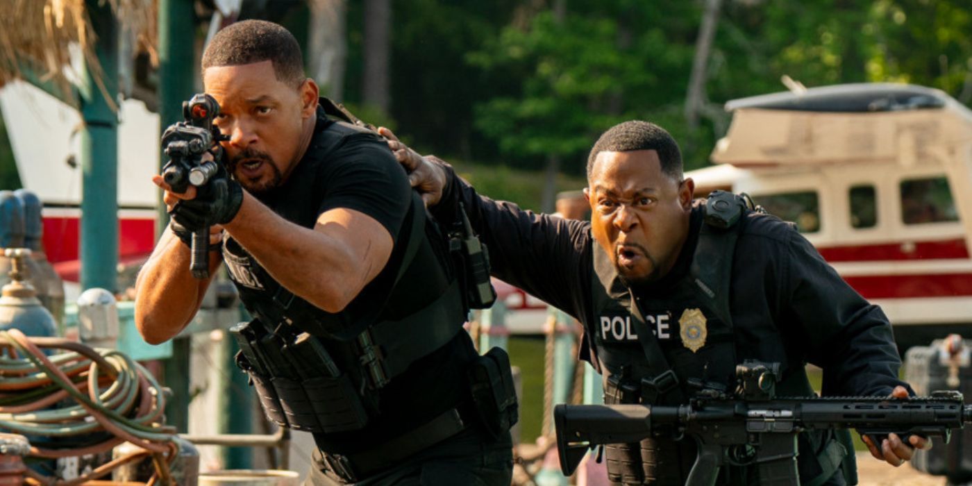 Will Smith points an assault rifle at a dock and Martin Lawrence stands next to him.