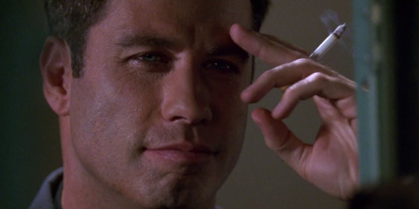 John Travolta as Vic Deakins smirks at someone off-screen while holding a lit cigarette in Broken Arrow 