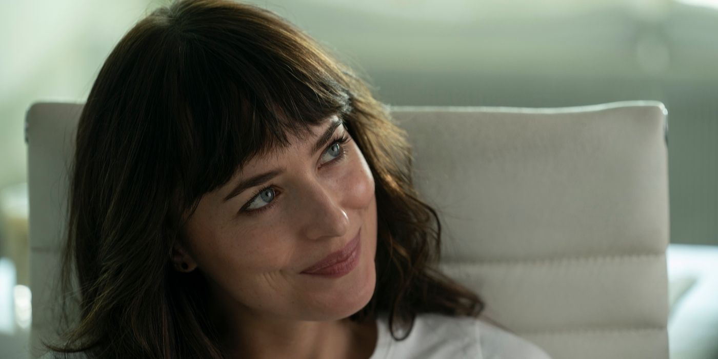 Dakota Johnson as Lucy sitting in an office chair and smiling in Am I Ok?