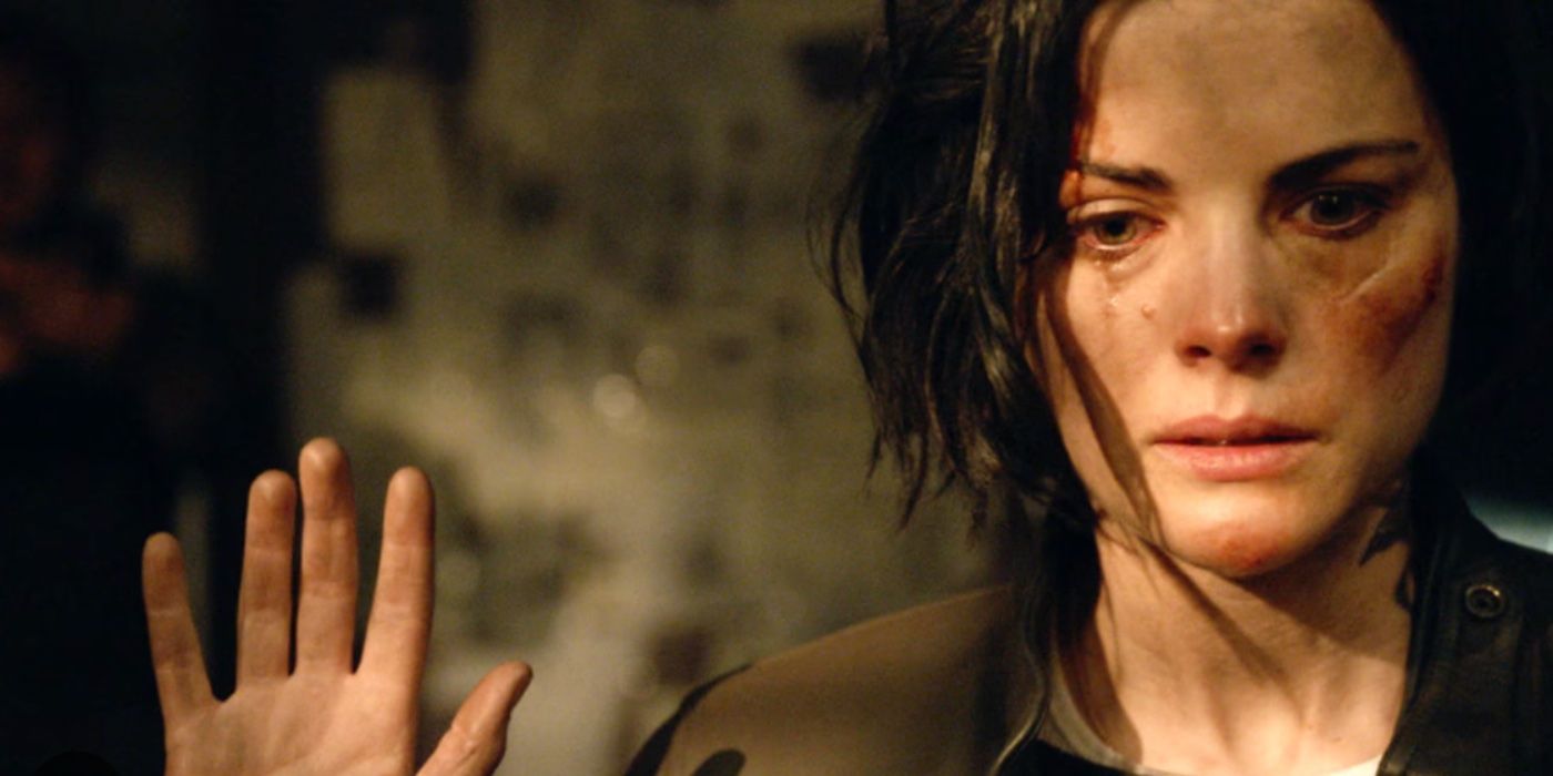 Jane solemnly surrenders with her arms slightly up in the air. A tear falls down her ash-stained cheek.