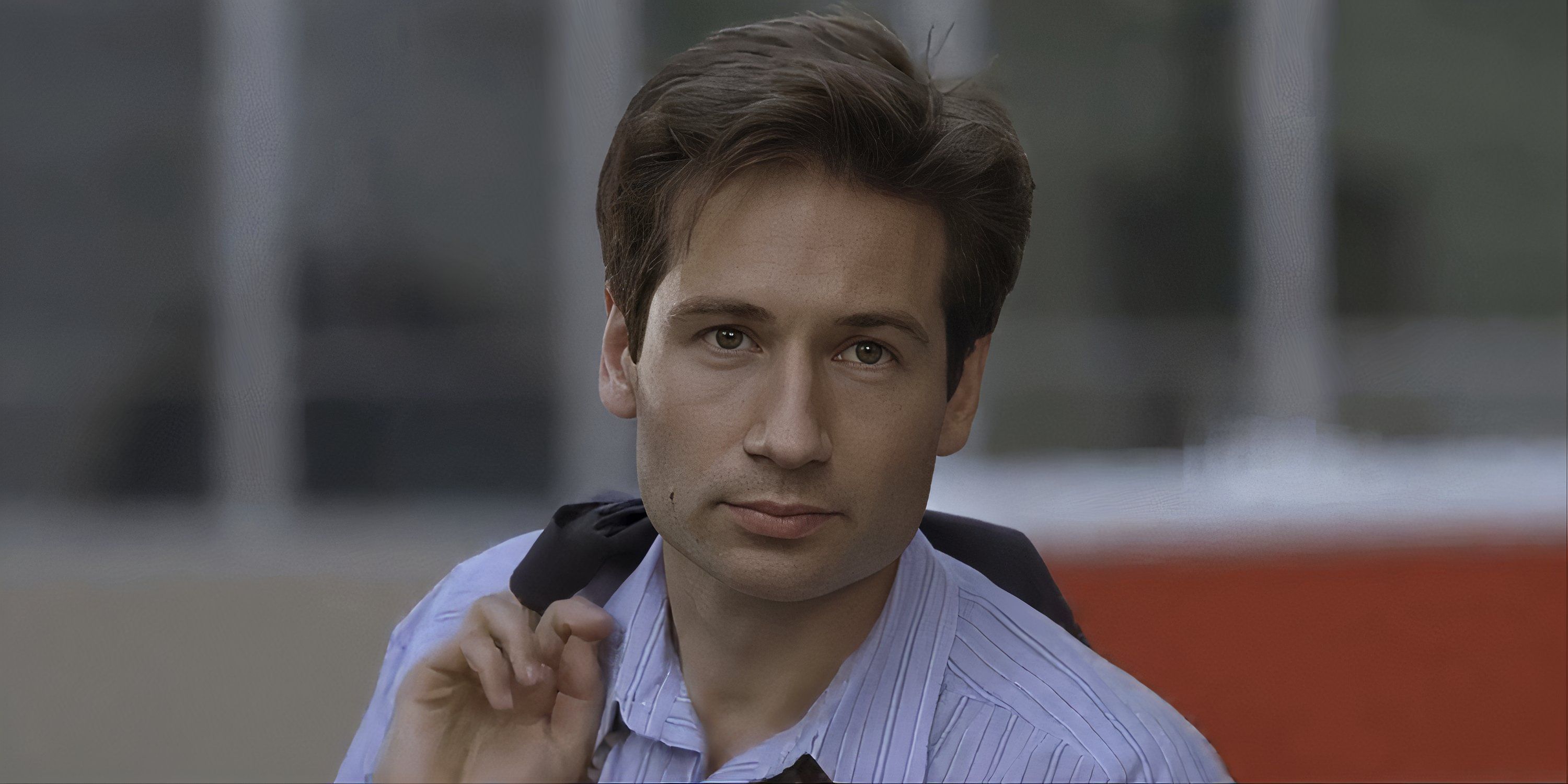 David Duchovny as Fox Mulder holding a jacket over his shoulder, and looking at something off-camera.