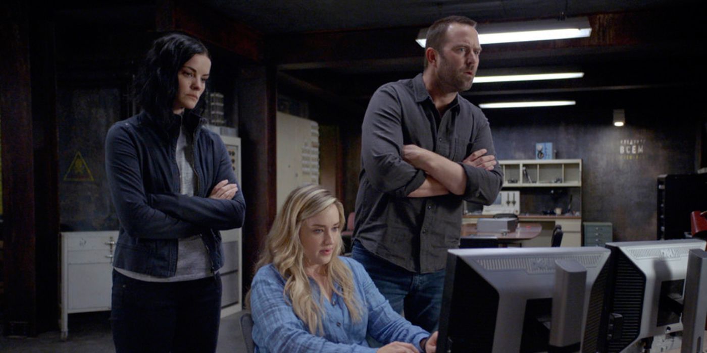Jane and Weller standing behind Patterson as they observe her typing into a computer.