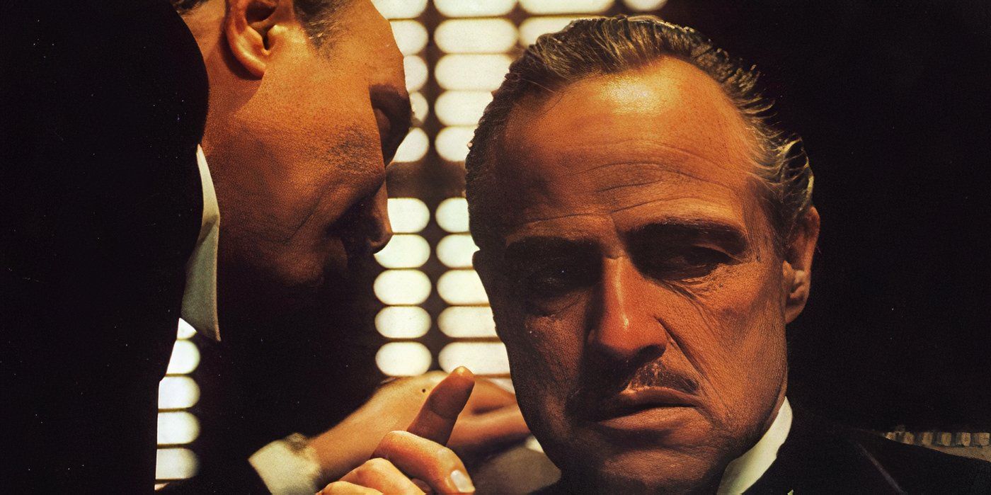 An associate of Vito Corleone (Marlon Brando) whispers in his ear as he smokes a cigar 