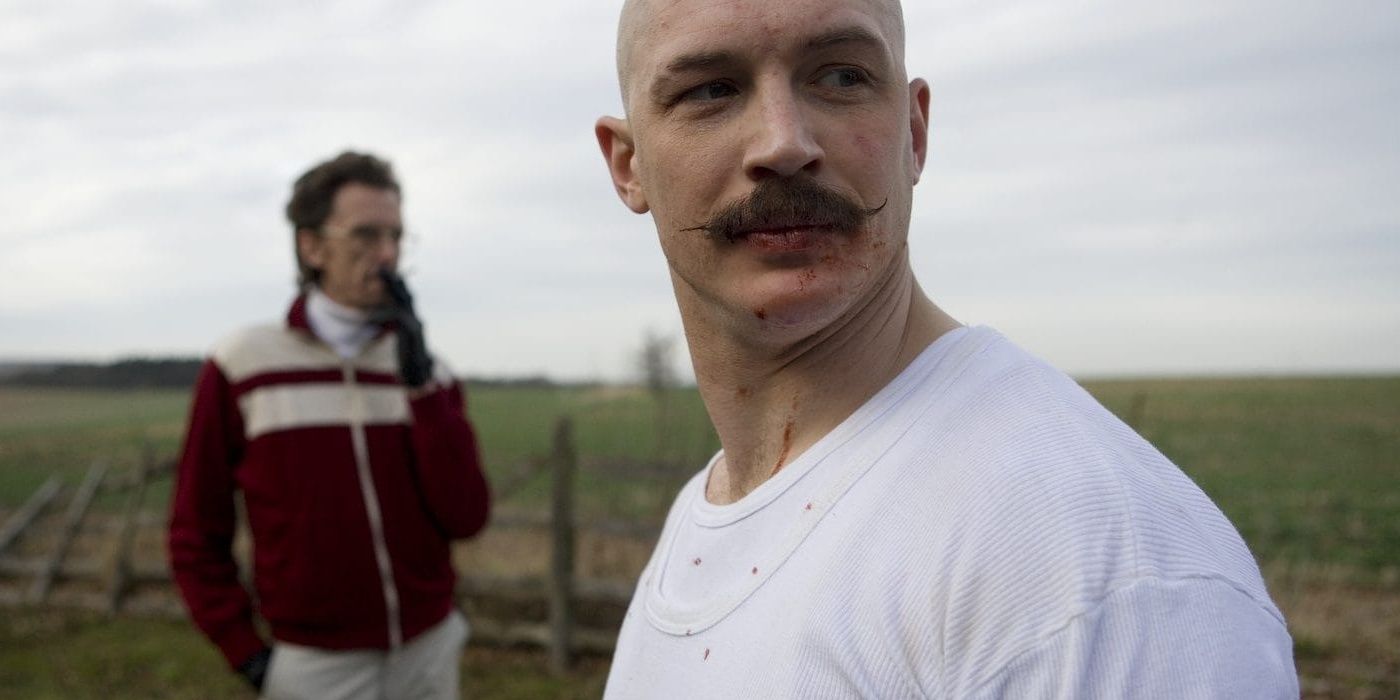 Bronson (Tom Hardy) looking to the distance while Paul (Matt King) stands in the background smoking in 'Bronson'
