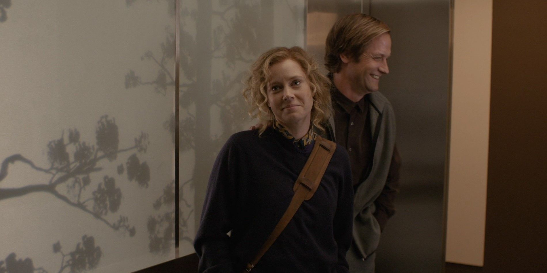 Amy smiling at someone while her husband Charles walks behind her in Her